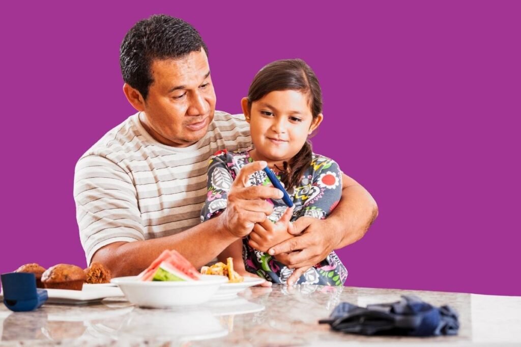 A father helps his young daughter manage her diabetes by showing her how to use a glucometer, with food placed on the table.