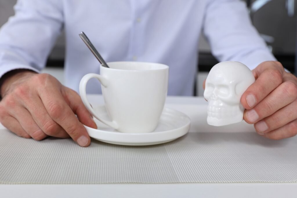 A person holding a white skull prop next to a cup of coffee, symbolizing the serious effects of hyperglycemia.