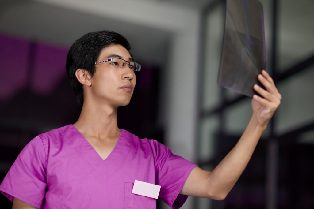 A healthcare professional in a purple medical uniform examines an X-ray film, carefully analyzing the results in a clinical setting.