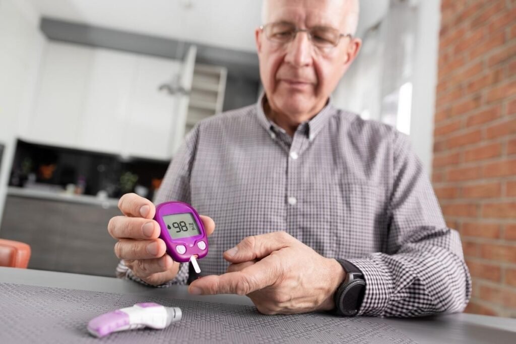 An elderly man checks his blood sugar level using a purple glucometer, showing a reading of 98 mg/dL, with an insulin pen placed on the table.