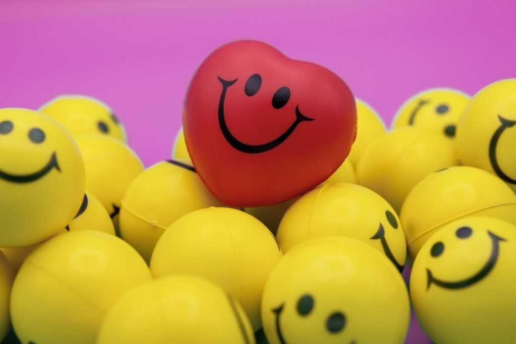 A red heart-shaped stress ball with a smiling face surrounded by yellow smiley face balls on a purple background.