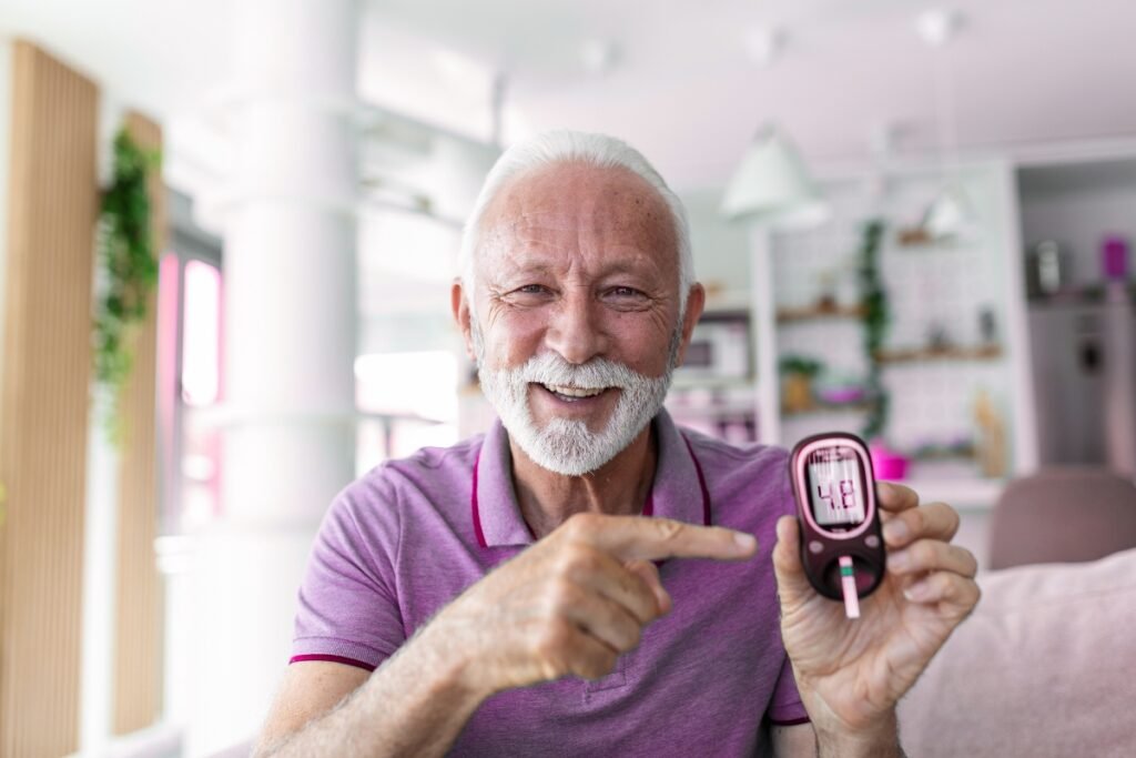 An elderly man smiles and shows his blood sugar reading of 4.8 mg/dL on a glucometer, indicating healthy diabetes management.